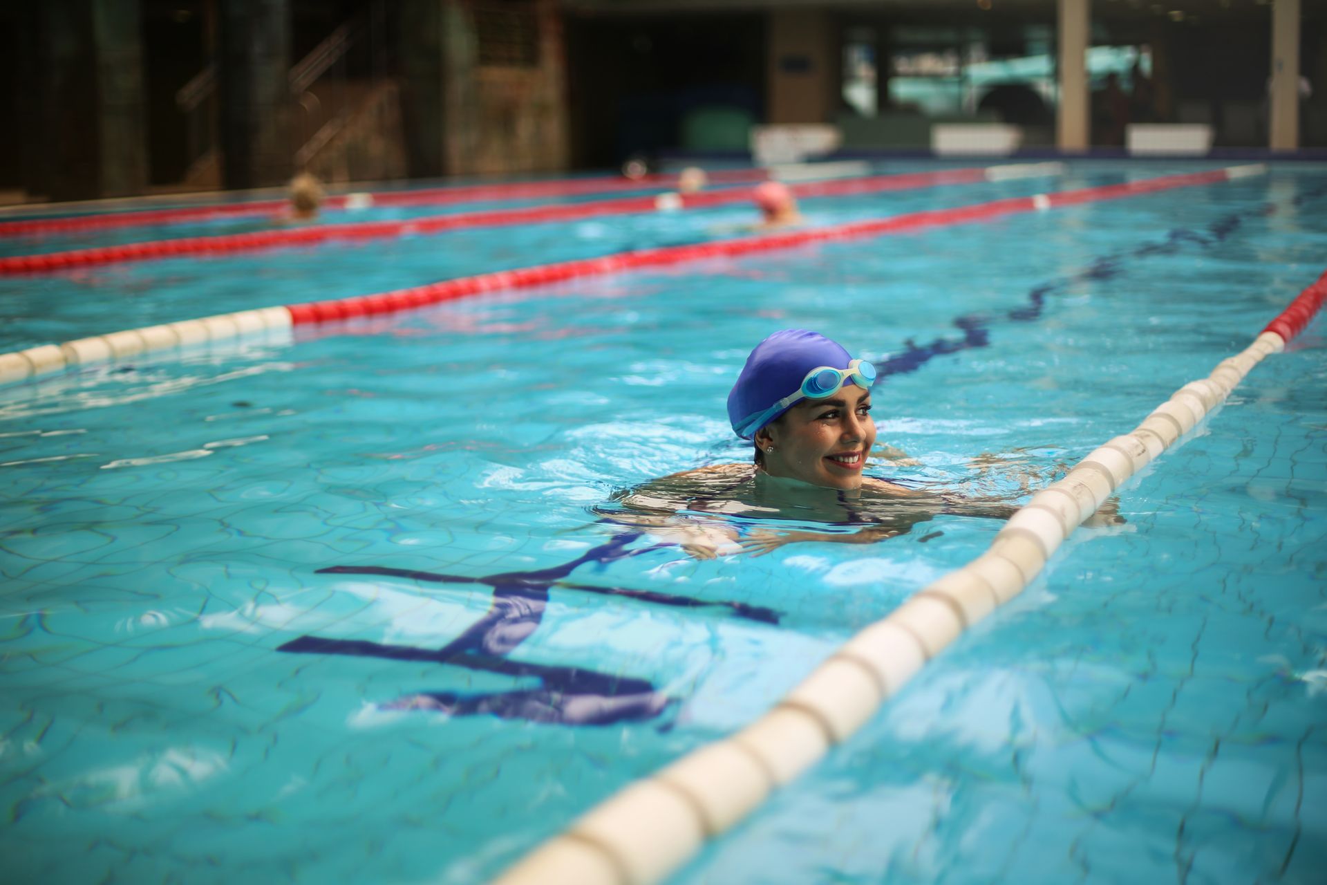 Lächelnde Schwimmerin mit Badekappe und Schwimmbrille im Hallenbad